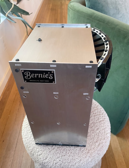 Aluminum box speaker with 'Bernie's' branding on a wooden floor.